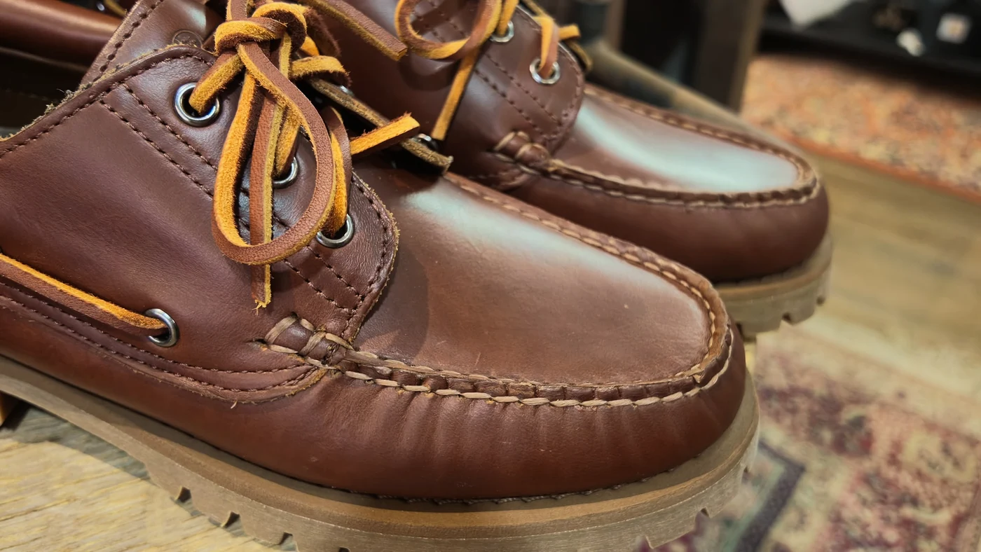 Pormenor das costuras e dos atacadores de um sapato Sebago castanho.